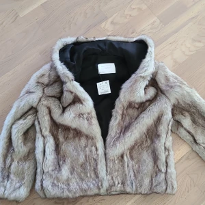 Beige fusk pälsjacka från Zara Woman - Snygg pälsjacka från Zara Woman i beige och bruna toner. Jackan har en fluffig, mjuk känsla och är helfodrad med svart tyg på insidan. Klassisk krage och stängs med diskreta hyskor framtill. Perfekt för dig som vill sticka ut med en trendig look.