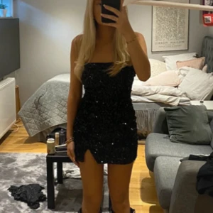 Svart paljettklänning NLY Trend S - Supersnygg svart kort klänning från NLY Trend, täckt med glittriga paljetter. Axelbandslös modell med figurnära passform och liten slits framtill. Perfekt för dig som vill sticka ut med en glamorös look.
