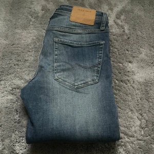 Blå slim fit jeans från Jack & Jones - Säljer ett par blå slim fit jeans från Jack & Jones, modell Glenn. Jeansen har klassisk femficksdesign, normal midja och snygg tvättad look. Perfekta för dig som gillar en smalare passform och tidlös stil.