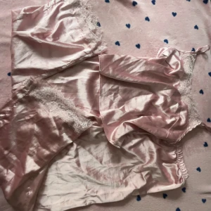 Rosa satin linnetopp med spets - Supersöt pjamas,  ljusrosa linnetopp och byxor i satin med tunnt material och vacker spetsdetalj upptill toppen och nertill på byxorna. Toppen och byxorna har en glansig finish och känns riktigt lyxig. Perfekt för dig som gillar romantisk och feminin stil. Inga hål och aldrig använt! Storlek står ej men jag är alltså 164 cm och storlek på kläder har jag 170 eller S/XS, skulle nog vilja säga att det är storlek S är inte säker men den passar mig sådär iallafall.