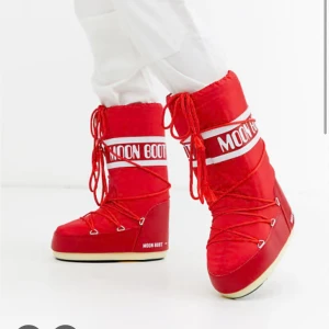 Röda Moon Boots med snörning - Säljer ett par ikoniska röda Moon Boots med vit logga och snörning framtill. Skorna har en rund tå, platt sula och är fodrade för extra värme. Perfekta för vintern och ger en riktigt retro vibe. Yttermaterialet är syntet och de har klassisk Moon Boot-design. Jag brukar ha storleken 39 i skor och de passar mig, kanske eventuellt något stora om nått ! Skorna är dessutom nästan aldrig använda💕💕