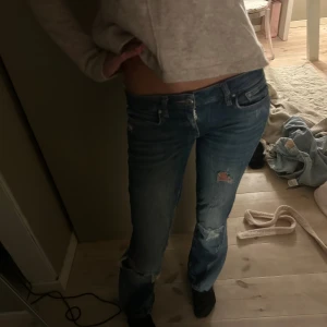Blå slitna jeans med låg midja - Säljer ett par blå jeans med slitningar och hål på knäna. De är sydda till bootcut och lågmidjade! AS snygga😍😍