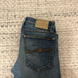 Blå jeans från Nudie Jeans - Snygga blå jeans från Nudie Jeans med klassisk femficksdesign och kontrastsömmar på bakfickorna. Perfekta för dig som gillar en smal siluett och stilren look. Hör av dig vid minsta lilla fråga!👍🏻W25 L32 jag ger Järna måtten för att nudies storlekar kan vara helt olika byxa till byxa. Passar dig runt 160 