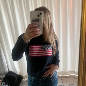 Mörkblå stickad tröja Meet Me There - Aldrig använd. Mörkblå stickad tröja från Meet Me There med amerikansk flagga framtill. Tröjan har rund halsringning, ribbade muddar och lång ärm. Perfekt för dig som vill ha en cool och avslappnad stil med en touch av USA-vibe.
