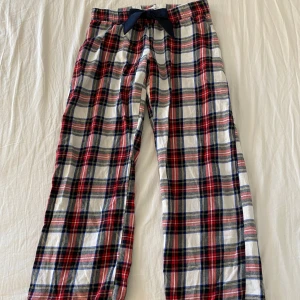 Rutig pyjamasbyxa från Gina Tricot - Mysiga pyjamasbyxor från Gina Tricot i röd, blå och vit rutig bomull. Byxorna har en mörkblå rosett framtill och resår i midjan för extra komfort. Perfekta för chill hemma eller sleepovers.😴😻