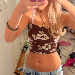 Hm topp - Säljer en brun croppad linnetopp med vita stora blommor. Toppen har tunna axelband i spets och sitter tight mot kroppen. Perfekt för sommarens varma dagar och ger en riktigt trendig Y2K-vibe.