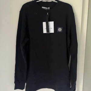 Navyblå sweatshirt från Stone Island - Snygg mörkblå sweatshirt från Stone Island med klassisk rund hals och ikonisk logopatch på bröstet. Tröjan har långa ärmar och ribbade muddar vid ärmslut och nederkant. Perfekt för dig som gillar stilrena och trendiga plagg.