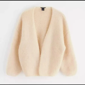 Beige fluffig kofta från & Other Stories - Supermjuk och oversized beige kofta från & Other Stories. Koftan är stickad med en öppen front och har långa, lite puffiga ärmar. Perfekt för lager-på-lager och ger en chill och mysig vibe till din outfit.