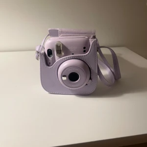 Instax Mini 11 - Snygg Instax Mini 11 i lila med matchande väska. Kameran är i mycket fint skick utan synliga repor eller slitage. Perfekt för att ta direktbilder och fånga minnen direkt på papper. Enkel att använda och smidig att ta med överallt.