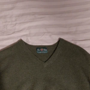 V-ringad tröja Alan Paine - Olivgrön v-ringad stickad tröja från Alan Paine i 100% ull. Klassisk modell med ribbade muddar och trekvartsärm. Perfekt för lager-på-lager och snygg till både jeans och kjol. Super Geelong-kvalitet för extra mjuk känsla. Storleken var från början L men den vart tvättad för varmt och krympte i tvätten. Så nu så är det omkring en S-M. Ärmarna från hand till axel 60cm. Nacke till midja 67cm. Har bara blivit använd max 3 gånger. Nypris 2000kr.