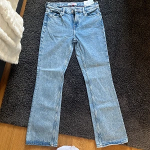 Ljusblå bootcut jeans Tommy Jeans - Säljer ett par ljusblå jeans från Tommy Jeans i klassisk bootcut-modell. Jeansen har fem fickor, normal passform och är tillverkade i denim av bomull. Perfekta för dig som gillar en retro vibe och vill ha ett par snygga jeans med lite utsvängda ben.