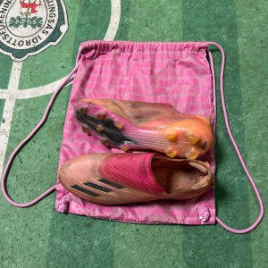 Adidas rosa fotbollsskor utan snörning - Säljer ett par Adidas fotbollsskor i en riktigt snygg rosa och orange färgskala med svarta detaljer. Skorna har en strömlinjeformad design utan snörning och mönstrad sula för bästa grepp på planen. Perfekta för dig som vill sticka ut och ha maxad känsla på fotbollen. Elite och jätte svåra att få tag på dom finns inte längre lite smutsiga bara 