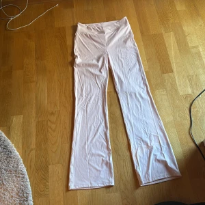 Ljusrosa utsvängda träningsbyxor Gina Tricot - Säljer ett par ljusrosa byxor från Gina Tricot med utsvängda ben och hög midja. Byxorna är i ett mjukt och stretchigt material som sitter snyggt och skönt. Byxorna har en v formad midja.