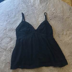 Svart linnetopp  - Säljer en svart linnetopp med smala axelband och v-ringning. Toppen har fina spetsdetaljer vid urringningen och nertill, jätte fin för sommaren. Köpte denna toppen men tyvärr passa inte mig så bra 