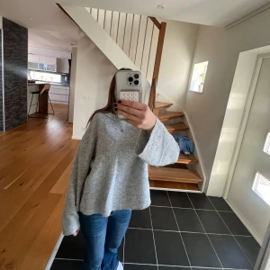 Grå stickad tröja från 157 - Mysig grå stickad tröja från 157 med avslappnad passform och breda ärmar. Tröjan har rund halsringning och är perfekt för lager-på-lager under kyliga dagar. Enkel och stilren design som funkar till jeans eller kjol.