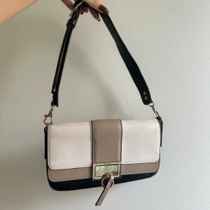 Aldo axelväska i svart, beige och vitt - Snygg axelväska från Aldo i svart, beige och vitt konstläder. Väskan har guldfärgade metalldetaljer, justerbart axelband och dragkedja på baksidan. Stilren design med rektangulär form och magnetlås framtill. Fin väska men guld detaljerna har börjat försvinna 