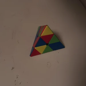 Pyraminx Triangular Rubik's Cube - Färgglad Pyraminx, en triangulär Rubik's Cube-liknande pussel. Bra skick, alla färger synliga och inga synliga skador. Perfekt för pusselentusiaster som vill ha en utmaning utöver den klassiska kuben.