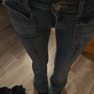 Mörkblå bootcut jeans med fickdetaljer - Säljer ett par mörkblå jeans med bootcut-modell och snygga framfickor. Jeansen har markerade sömmar längs benen och klassisk knappgylf. Perfekta för dig som gillar en tidlös look med lite extra edge.