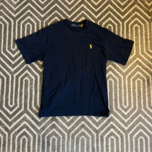 Marinblå t-shirt från Polo Ralph Lauren - Klassisk marinblå t-shirt från Polo Ralph Lauren med gul broderad logga på bröstet. Riktigt snygg, använd 2 gånger och säljer den för att den inte passar. Nypris: ca 800kr. Tveka inte på att skriva ifall du undrar nåt!✨