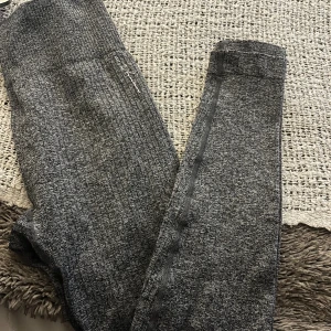 Grå ribbade leggings från Nelly - Mörkgrå ribbade leggings från Nelly med diskret logga vid höften. De är stretchiga och har hög midja, perfekta för träning eller chill. Materialet är mjukt och följsamt, vilket gör dem riktigt bekväma att bära hela dagen.