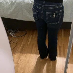 Mörkblå bootcut jeans med kontrastsömmar - Snygga mörkblå jeans med tydliga vita kontrastsömmar och bootcut passform. Byxorna har klassiska fickor med lock och knappdetaljer bak, samt låg midja. Storleken ör 158 och byxorna är ej använda. Pris går att diskuteras! 🥰