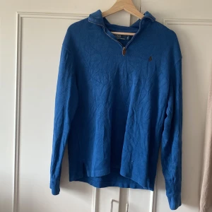 Blå half zip tröja Polo Ralph Lauren - Blå långärmad tröja från Polo Ralph Lauren med klassisk broderad logga på bröstet. Tröjan har en snygg krage med half zip-dragkedja och är tillverkad i mjuk bomull. Perfekt för lager-på-lager och chill stil.