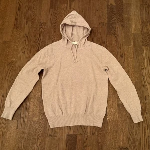 Beige hoodie i mjuk kashmir från Sayless - Säljer en stilren beige hoodie i mjuk kashmir med huva och snörning. Tröjan har långärmade ribbade muddar och ribbad nederkant, perfekt för dig som gillar en clean och chill look. Passformen är normal och materialet känns lyxigt mot huden.
