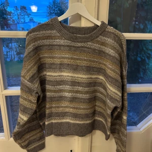 Randig stickad tröja från Pull&Bear - Mysig stickad tröja från Pull&Bear i gråa och beige toner med randigt mönster. Tröjan har rund halsringning, ribbade muddar och lång ärm. 