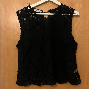 Svart spetstopp - Supersnygg svart blus köpt i en butik i Smögen. Ärmlös modell med inbygdd tubtop som täcker bara en del så man ändå ser spetsen.storlek L/XL men skulle säga att den passar allt från S beroende på hur man vill att den ska sitta!