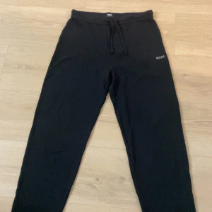 Svarta mjukisbyxor från BOSS - Svarta mjukisbyxor från BOSS med diskret logga på vänster höft. Byxorna har snörning i midjan och är tillverkade i mjukt material som känns skönt mot huden. Perfekt för chill eller häng med kompisar.