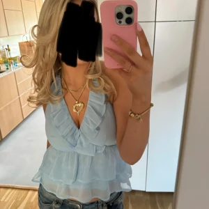 Ljusblå volangig blus med knyt - Supersöt ljusblå blus med volanger och v-ringning. Toppen har omlott-design framtill och knyt i nacken.