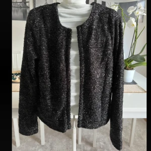 Glittrig svart kofta från Vila - Säljer en svart glittrig kofta från Vila i storlek S. Koftan har lång ärm, öppen framtill och är tillverkad i ett glittrigt, mjukt material som ger en festlig känsla. Perfekt att slänga över en topp för att lyfta din look.
