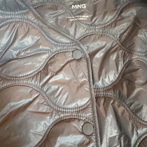 Grå quiltad pufferjacka från MNG MANGO - Säljer en grå pufferjacka från MNG med snyggt quiltat mönster och rundade former. Jackan har knappar framtill och en kort, boxig passform som ger en cool vibe. Perfekt för dig som gillar stilrena och moderna jackor. Storlek XXL men som en normal L