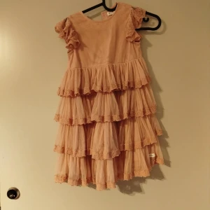 Rosa volangklänning med spetsdetaljer - Supersöt rosa klänning med flera lager volanger och spetsdetaljer på både ärmar och kjol. Klänningen har korta volangärmar och en rund halsringning. Perfekt för dig som vill sticka u med en romantisk och lekfull stil newbie klänning storlek 122