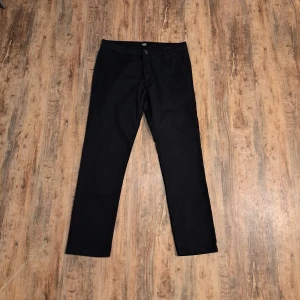 Svarta chinos - Lager 157 - Svarta chinos från 157 med klassisk rak passform och midwaist. Byxorna har sidofickor fram och diskreta fickor bak. Materialet är mjukt och känns som bomull, perfekt för en clean och enkel look. Stängs med knapp och dragkedja i midjan.