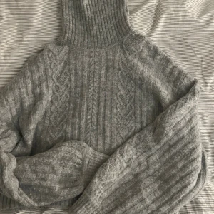 Grå polotröja från H&M, stickad S - Säljer en grå stickad polotröja från H&M i storlek S. Tröjan har ett snyggt kabelstickat mönster och ribbad polokrage som ger extra mysfaktor. Perfekt för kyliga dagar och enkel att matcha med jeans eller kjol.