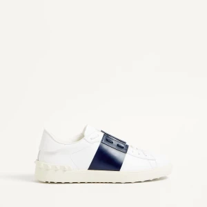 Valentino Garavani Open sneakers vit/blå - Snygga Valentino Garavani Open sneakers i vitt skinn med bred marinblå läderdetalj över snörningen. Klassisk låg modell med rund tå, vita snören och ikoniska nitar på sulan. Perfekta för dig som gillar stilrena och exklusiva sneakers.