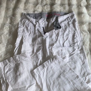 Linne byxor  - Säljer ett par vita byxor från Kilgen Denim med snörning i midjan och dragkedja. Byxorna har flera fickor och är tillverkade i ett lätt bomullsmaterial, perfekta för en avslappnad stil. Snygga detaljer med sömmar och randigt innerfoder i midjan.