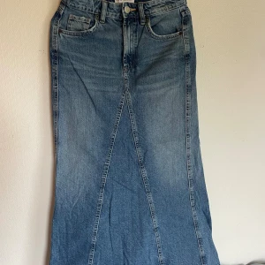 Blå denim kjol Zara  - Snygg lång jeanskjol i klassisk blå denim med femficksmodell och hög midja. Kjolen har en lätt utsvängd form och markerade sömmar framtill som ger en cool vintagekänsla. Perfekt att styla med sneakers eller boots.