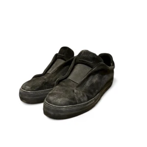 Svarta mocka sneakers från ARIGATO - Svarta sneakers från ARIGHT i mjuk mocka med platt sula och rund tå. Skorna har en minimalistisk design utan snörning och en diskret logga på sidan. Perfekt för dig som gillar stilrena och enkla skor med en urban vibe.