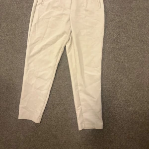 Beiga högmidjade kostymbyxor - Snygga beiga kostymbyxor med hög midja och raka ben. Byxorna har diskreta fickor framtill och är sydda i ett mjukt material som ger en clean och stilren look. Perfekta för dig som gillar en klassisk och enkel stil.