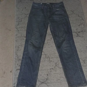 Blå raka jeans i storlek 164 - Klassiska blå jeans med rak passform och fem fickor. Jeansen har en enkel design utan synliga detaljer och är tillverkade i ett tåligt denimtyg. Perfekta för dig som gillar en tidlös stil.