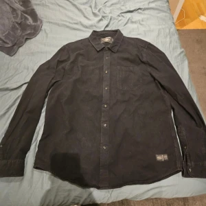 Svart skjorta från Scotch & Soda XXL - Svart skjorta från Scotch & Soda i storlek XXL men sitter som L. Klassisk modell med bröstficka, knappar framtill och krage. Skjortan är tillverkad i mjuk bomull och har en stilren look som passar perfekt till jeans eller chinos.