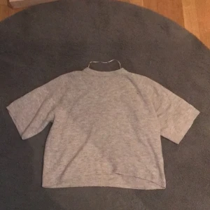 Beige stickad kortärmad tröja från lager157 - En enkel och stilren beige stickad tröja med korta ärmar och rak passform. Tröjan har en högre halsringning och är gjord i mjukt material som känns skönt mot huden. Perfekt för lager-på-lager under höst och vinter. Har ett synligt hål på framsidan av tröjan.