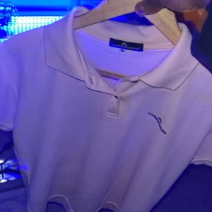 Ljusrosa pikétröja från J.Lindeberg - Snygg ljusrosa pikétröja från J.Lindeberg med klassisk krage och korta ärmar. Tröjan har diskret logga broderad på bröstet och är gjord i mjuk bomull som känns skön mot huden. Perfekt för en chill och stilren look.