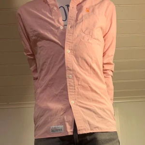 Ljusrosa skjorta från Sail Racing - Unik ljusrosa skjorta från Sail Racing med klassisk krage, knappstängning och bröstficka med orange logodetalj.  Slim passform som sitter perfekt.  Tveka inte på att skriva ifall du undrar nåt!✨