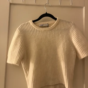 Ribbad beige topp från Zara - Säljer en ribbad topp från Zara i storlek L. Toppen är beige, har rund hals och korta ärmar. Materialet är stickat och ger en mysig känsla. Perfekt för dig som gillar enkel och stilren design med lite struktur. Den är croppad