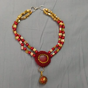 Färgstarkt halsband med pärlor och berlock - Unikt halsband med röda och guldiga pärlor i olika former, samt en rund röd mittdel med glittrig effekt. Hängande berlock i guld och rött med öppningsbar design och en fluffig röd boll, som kan sprayas med favorit parfymen. Perfekt för dig som gillar färg och detaljer. 