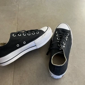 Svarta Converse All Star sneakers - Klassiska svarta Converse All Star sneakers med vit tå och sula. Låga med snörning, silverfärgade öljetter och canvasmaterial. Perfekta för en avslappnad och cool stil. Ikonisk logga baktill och platt sula för skön känsla.