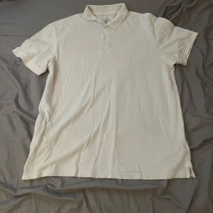 Vit pikétröja från L.O.G.G. - Snygg vit pikétröja från L.O.G.G. med klassisk krage och två knappar framtill. Tröjan har korta ärmar och är gjord i mjuk bomull som känns skön mot huden. Perfekt för dig som gillar enkel och clean stil.